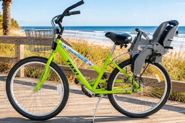 Green bike with child seat parked on boardwalk by the beach.