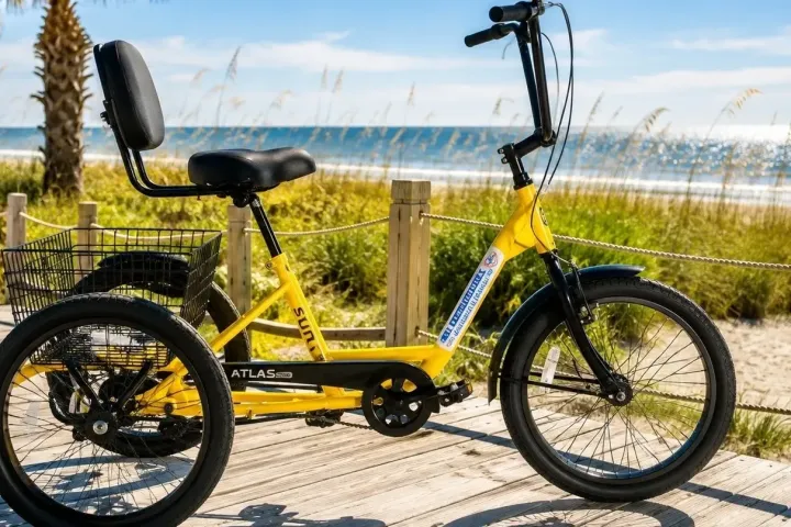 Yellow tricycle with a basket on a boardwalk by the beach.
