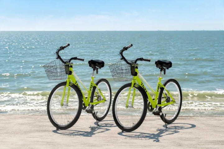 Two yellow bicycles with baskets on a boardwalk by the sea.
