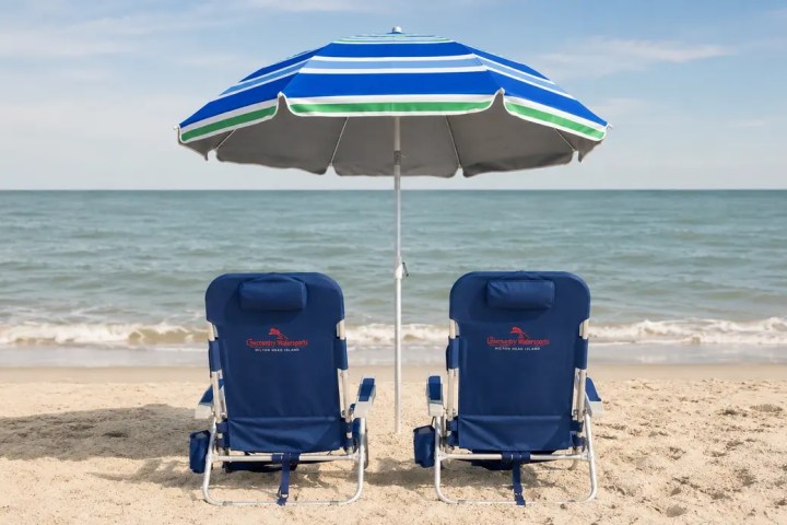 Two blue beach chairs under a striped umbrella on a sandy beach.