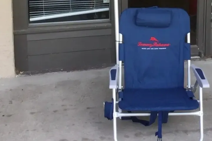 Blue beach chair with a pillow outside a storefront on a sidewalk.