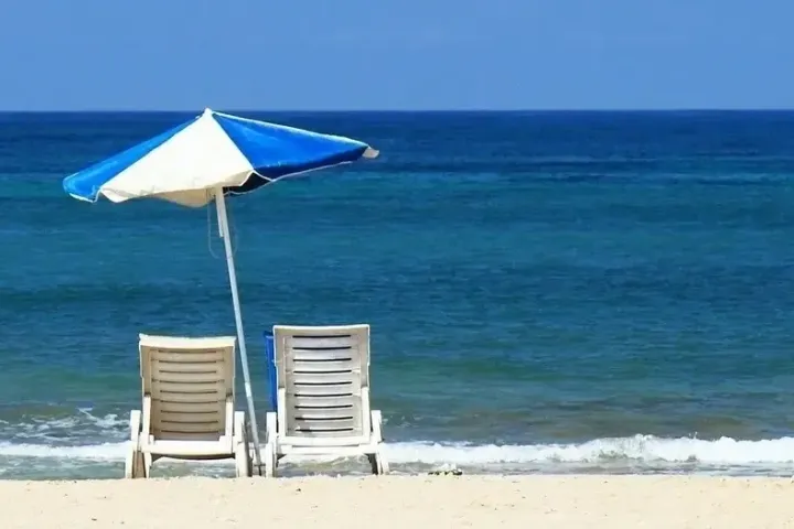 Two beach chairs and blue umbrella on a sandy shore facing the ocean.